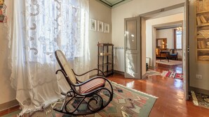 A room with a rocking chair, a patterned rug, and a door leading to another room. - Orazio Liberty House, Lunigiana, Nature (Fivizzano)