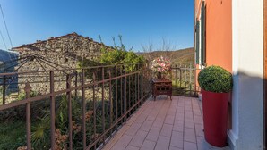 A balcony with a stone building in the background, a metal railing, and a potted plant. - Orazio Liberty House, Lunigiana, Nature (Fivizzano)