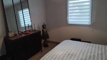 Een slaapkamer met een bed, een dressoir, een spiegel, een raam en een beeld.