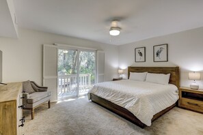 Quarto com uma cama grande, uma escrivaninha, uma cadeira, um ventilador de teto e uma varanda com vista para árvores.