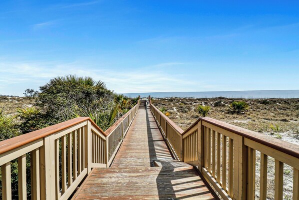 A wooden boardwalk leading to a beach with a clear view of the ocean.