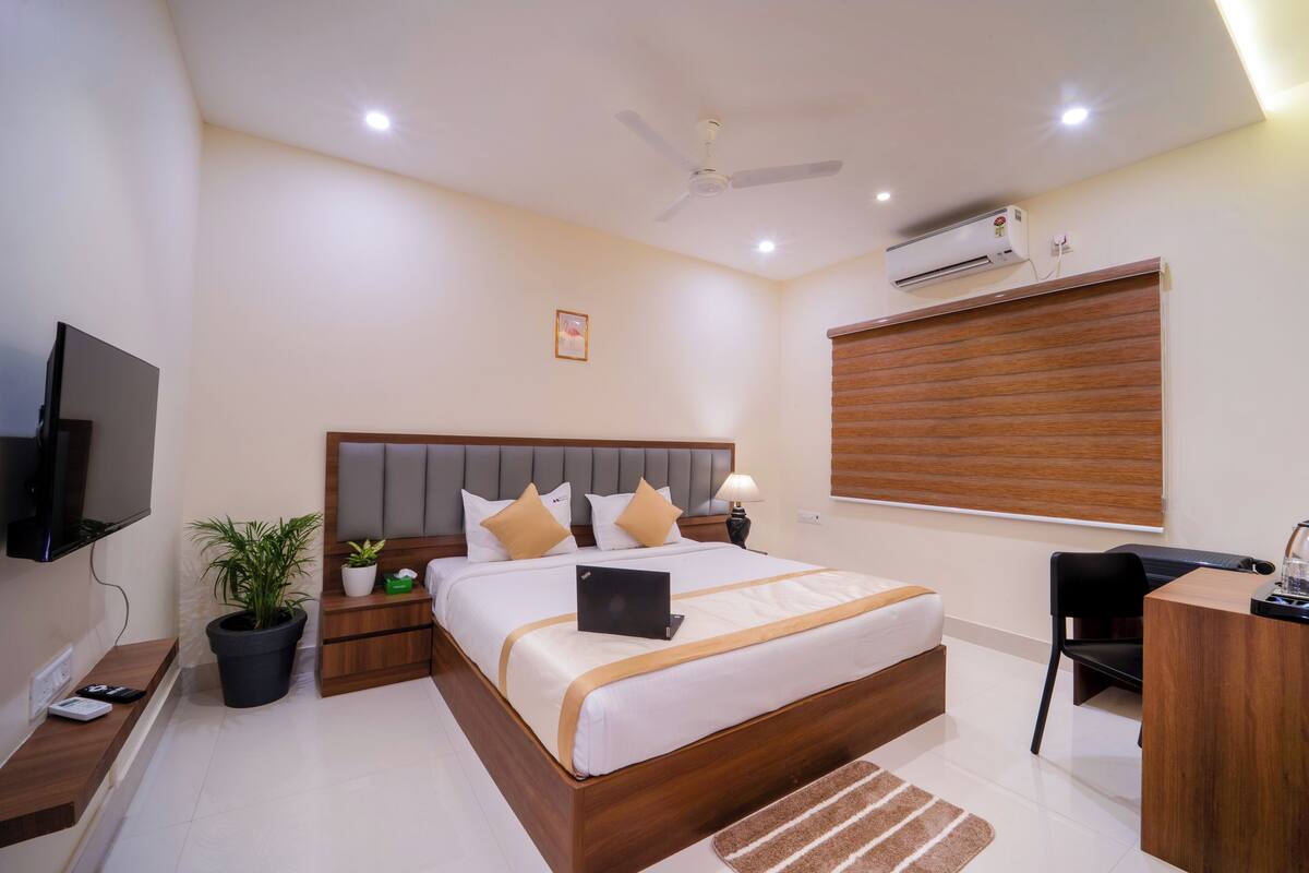 A modern hotel room with a large bed, a desk, a TV, and an air conditioning unit.