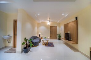Una sala de estar moderna con un sofá, una mesa de centro, un televisor sobre una estantería de madera, una planta en maceta y una mesita con una lámpara.
