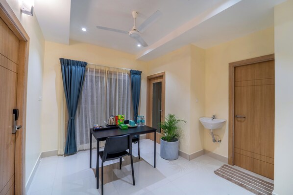 A room with a dining table, chairs, a ceiling fan, a potted plant, a sink, and a wooden door. - Mcity Elite Suites (Chengalpattu)