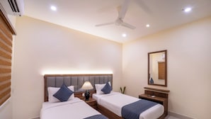 Une chambre d’hôtel avec deux lits, un ventilateur de plafond, une table de chevet avec une lampe et un miroir au mur.