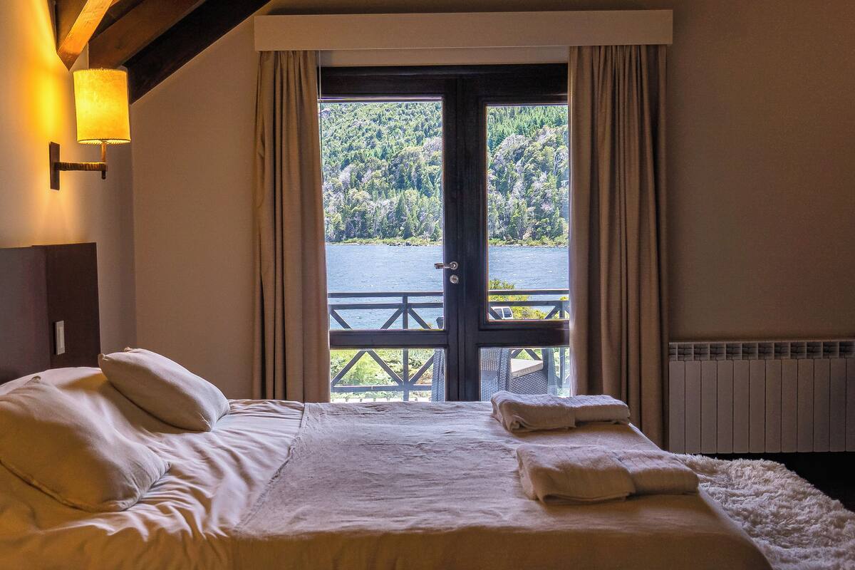 Un dormitorio con una cama grande, vistas a un lago y un techo de madera.