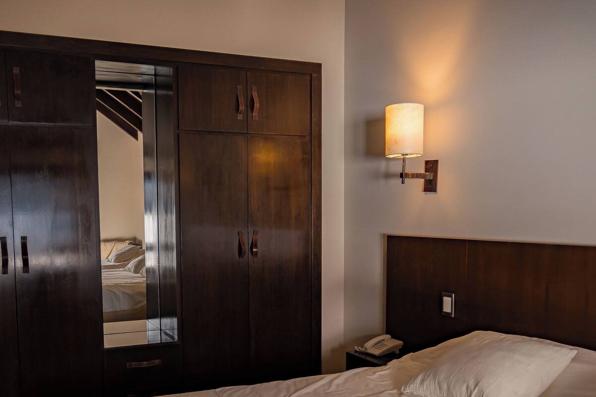 Una habitación de hotel con un armario grande, una mesita de noche con lámpara y una cama con toallas.