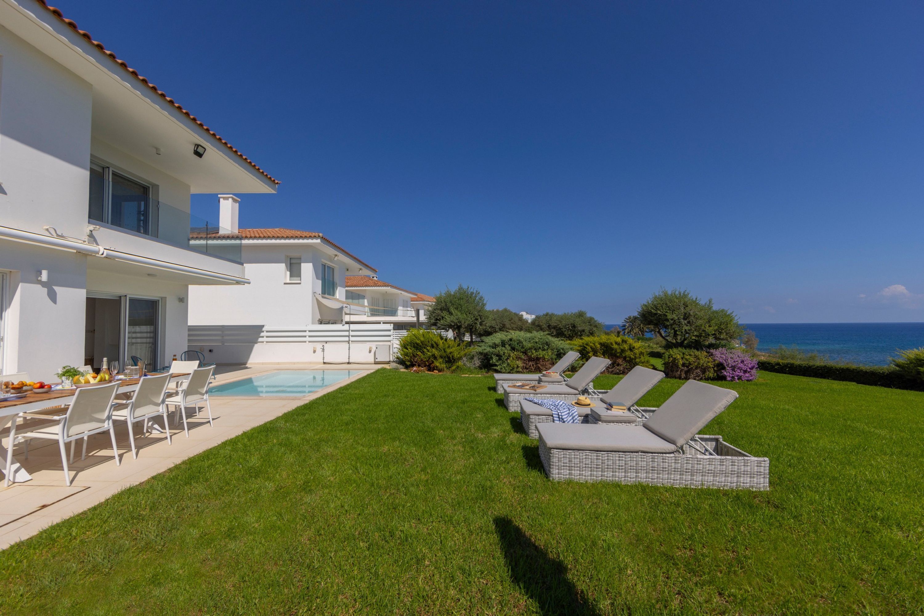 A modern house with a swimming pool, outdoor seating, and a view of the sea.