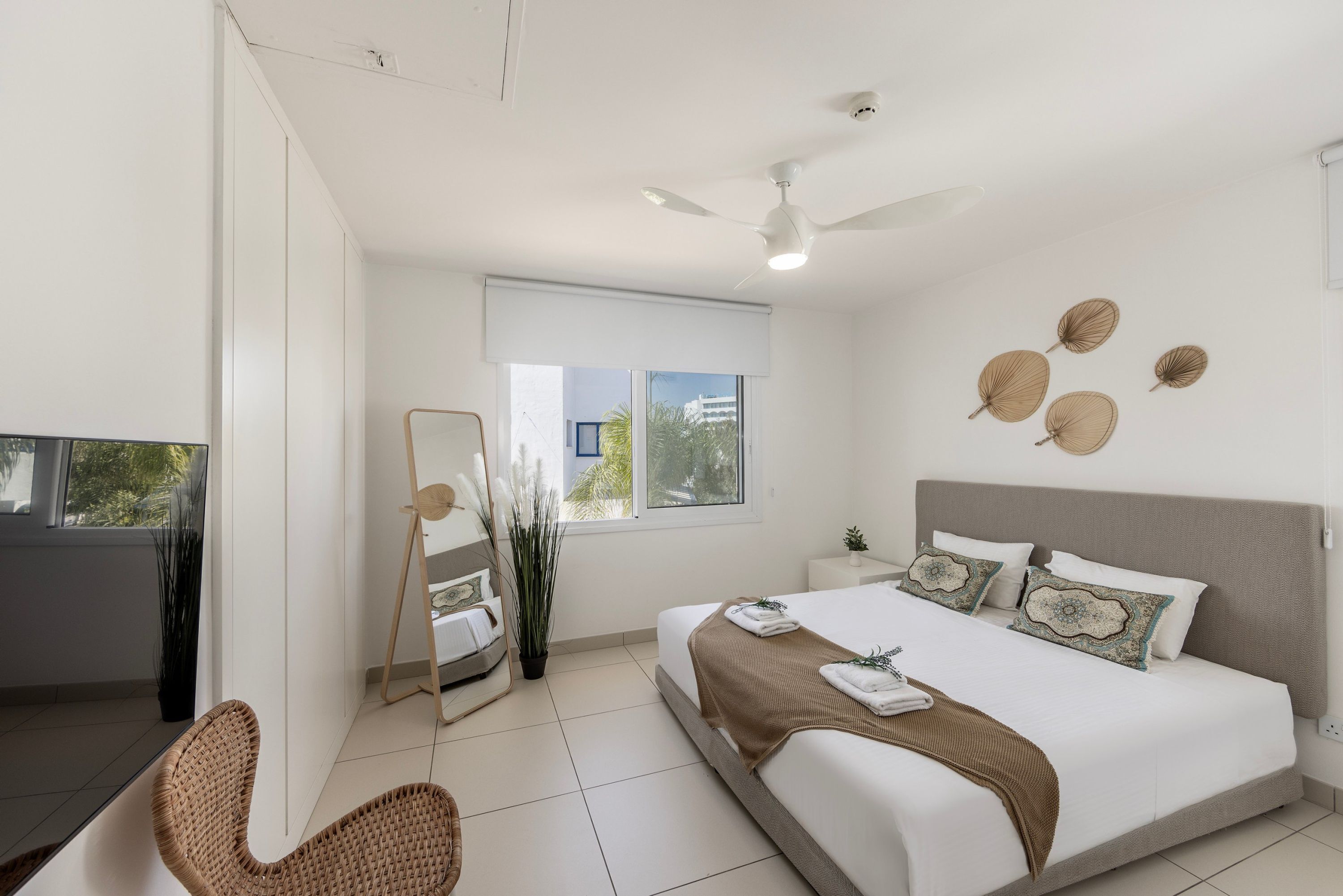 A modern bedroom with a large bed, a ceiling fan, a window with a view, and a small bedside table.