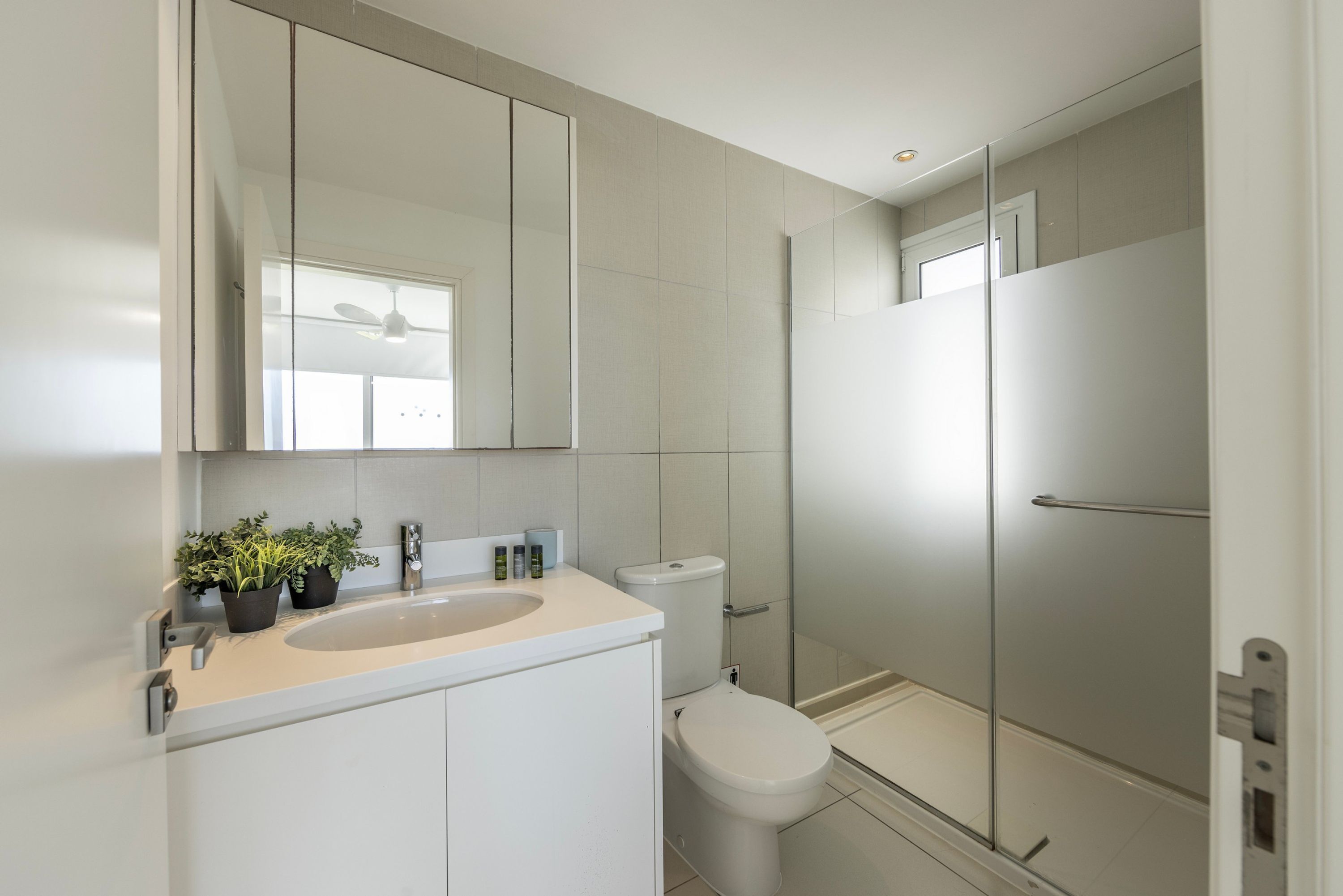 A modern bathroom with a sink, mirror, toilet, and glass shower enclosure.