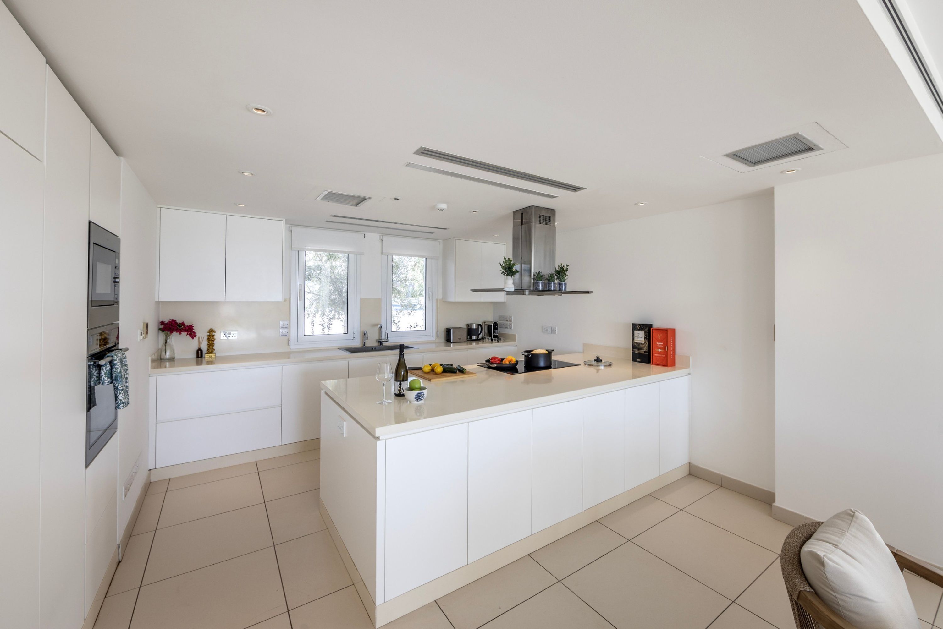 Une cuisine moderne avec des meubles blancs, un îlot central et une cuisinière intégrée.