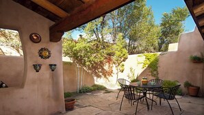 Un patio al aire libre con una mesa y sillas, rodeado de muros con detalles decorativos y plantas en macetas.