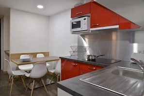 Una cocina compacta con microondas, pileta de acero inoxidable y un comedor con mesa y sillas.