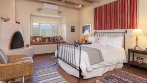 Une chambre à coucher avec un lit, un coin fenêtre, une cheminée, un ventilateur de plafond et une décoration murale à rayures.