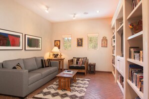 A living room with a grey sofa, a small table with a lamp, a chair, and a bookshelf filled with books.