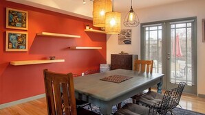 Un espace repas comprenant une table en bois, des chaises, des luminaires suspendus et des œuvres d’art accrochées aux murs.