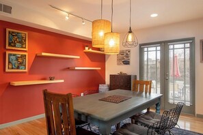Zona pranzo con tavolo in legno, sedie, lampadari e opere d'arte alle pareti.