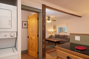 A compact living space with a washing machine, a wooden door, a sofa, a coffee table, and a ceiling fan.