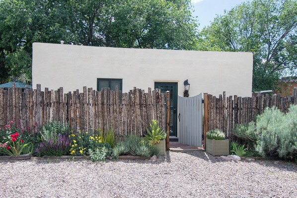 A building with a wooden fence, a gravel driveway, and a variety of plants.