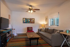 A living room with a television, a ceiling fan, a sofa, a coffee table, and a window.