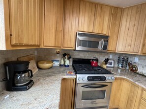 A kitchen with wooden cabinets, a stainless steel microwave, a gas stove, a coffee maker, and various kitchen utensils.