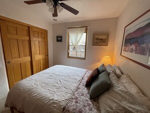 A bedroom with a bed, a window with curtains, a ceiling fan, and a framed picture on the wall.