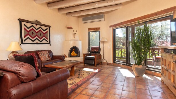 Una sala de estar acogedora con chimenea, muebles de cuero y un amplio ventanal con vistas a la vegetación.