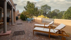 Un patio al aire libre con sillones, una mesa y una parrilla.