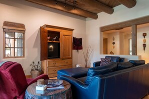 A living room with a blue sofa, a red armchair, a wooden cabinet, and a round glass table with a book and a vase.