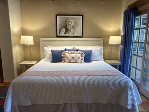 Una camera d'albergo con un letto grande, due lampade ai comodini, un quadro appeso al muro e una finestra con tende.