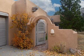 A stucco house with a gray gate, a mailbox, and a tree with autumn leaves.