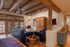 A spacious living room with a fireplace, leather sofas, a wooden cabinet, and a ceiling fan.