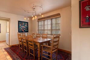 A dining area with a wooden table and chairs, a patterned rug, a ceiling light fixture, and a window with blinds.