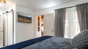 Quarto com cama, vista para paisagem pela janela e porta que dá para um banheiro.