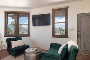 A living room with two green sofas, a round coffee table, and a flat-screen TV mounted on the wall.