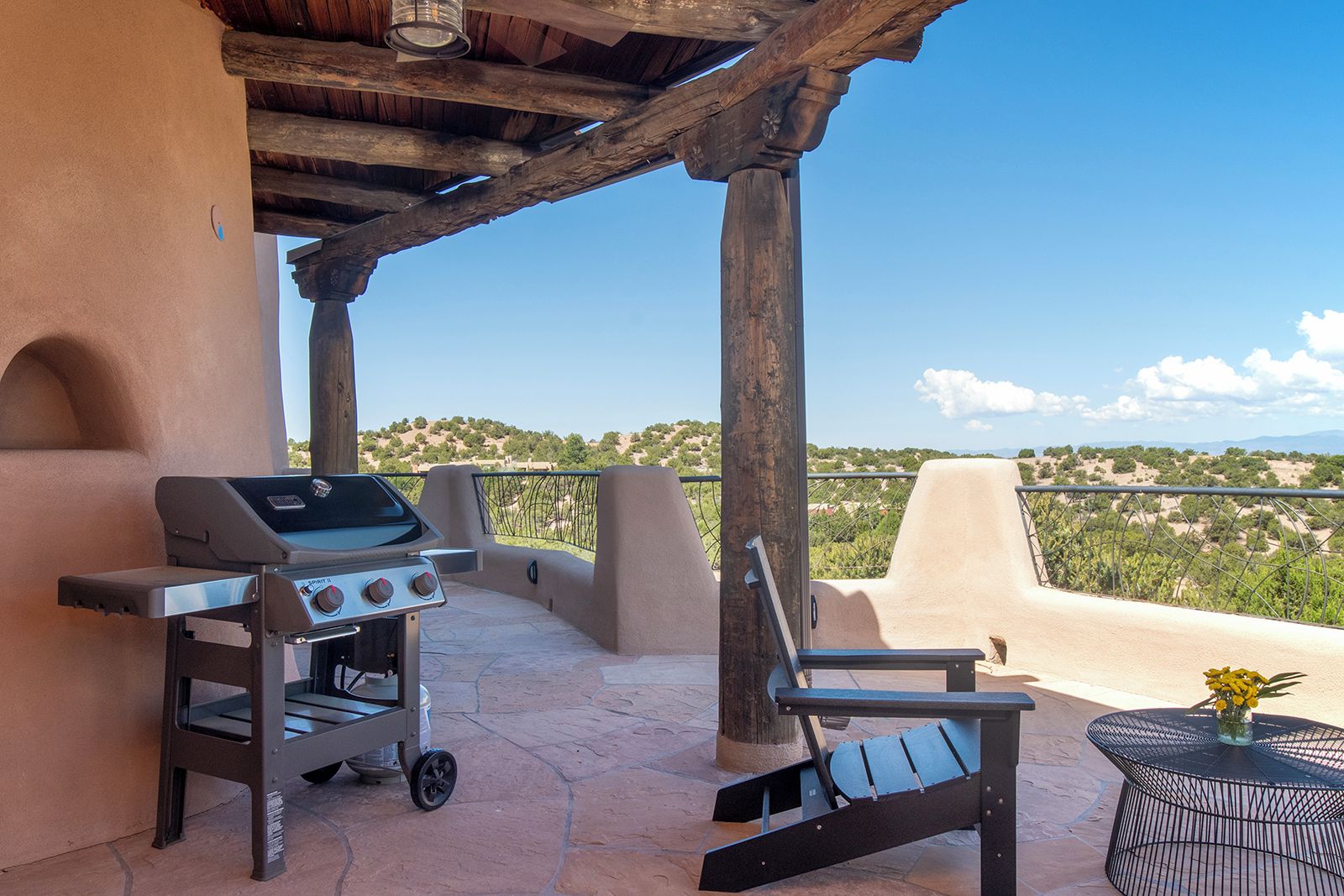 An outdoor patio with a barbecue grill, a chair, and a table with a vase of flowers.