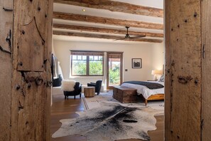 Un dormitorio con cama, techo de madera, ventana y alfombra de cuero de vaca.