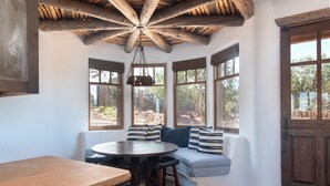 A cozy corner seating area with a round table and chairs, large windows with curtains, and a wooden ceiling. - Starry Night at the Opera (Santa Fe)