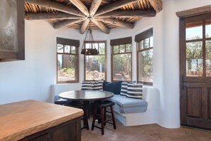 Un'accogliente area salotto con un tavolino rotondo e sedie, ampie finestre con tende e un soffitto in legno.