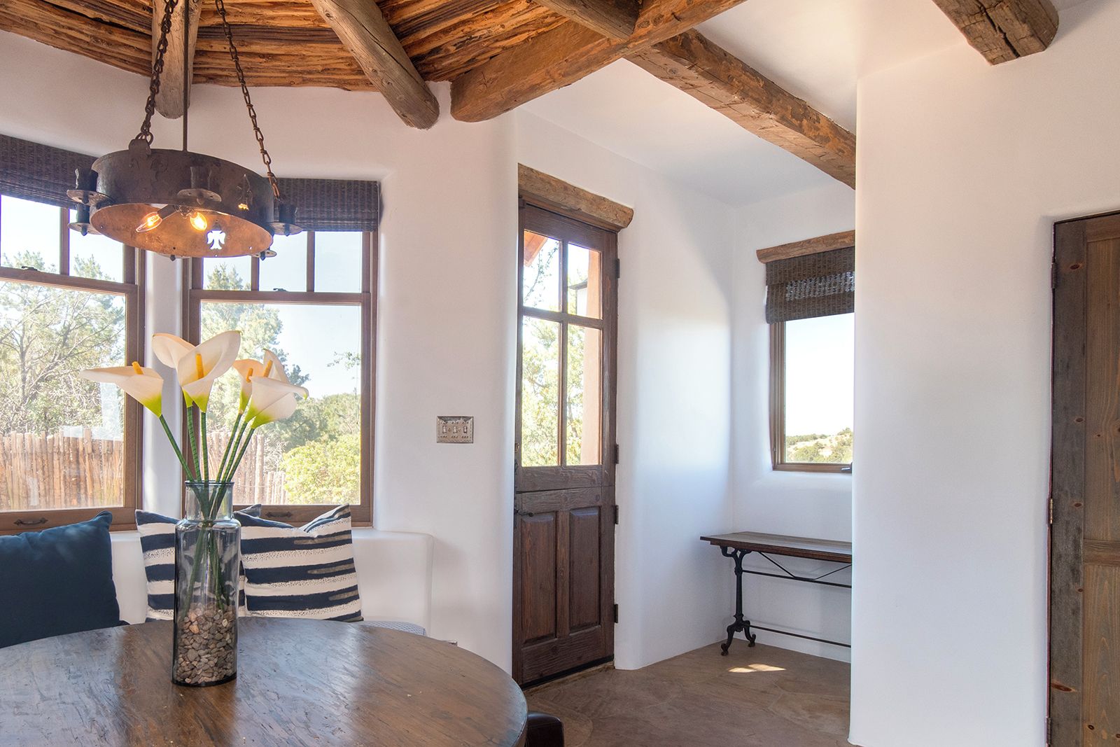 A room with a wooden ceiling, a round table with a vase of flowers, and a window with a view of trees.
