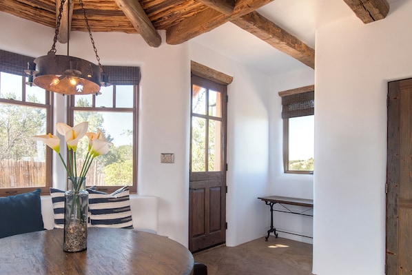 A room with a wooden ceiling, a round table with a vase of flowers, and a window with a view of trees.