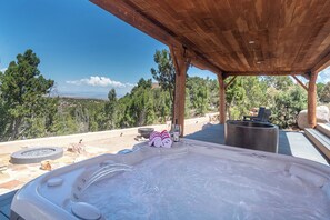 Una vasca idromassaggio con una pergola in legno sopra, circondata da un patio in pietra, con vista su un paesaggio montuoso.