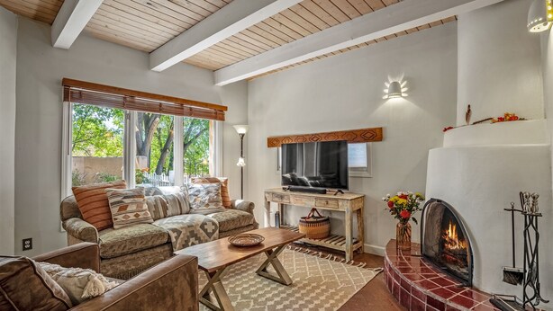 Een woonkamer met een open haard, een televisie en een groot raam met uitzicht op bomen.