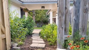 A garden pathway leading to a house with a covered porch and a wooden fence.