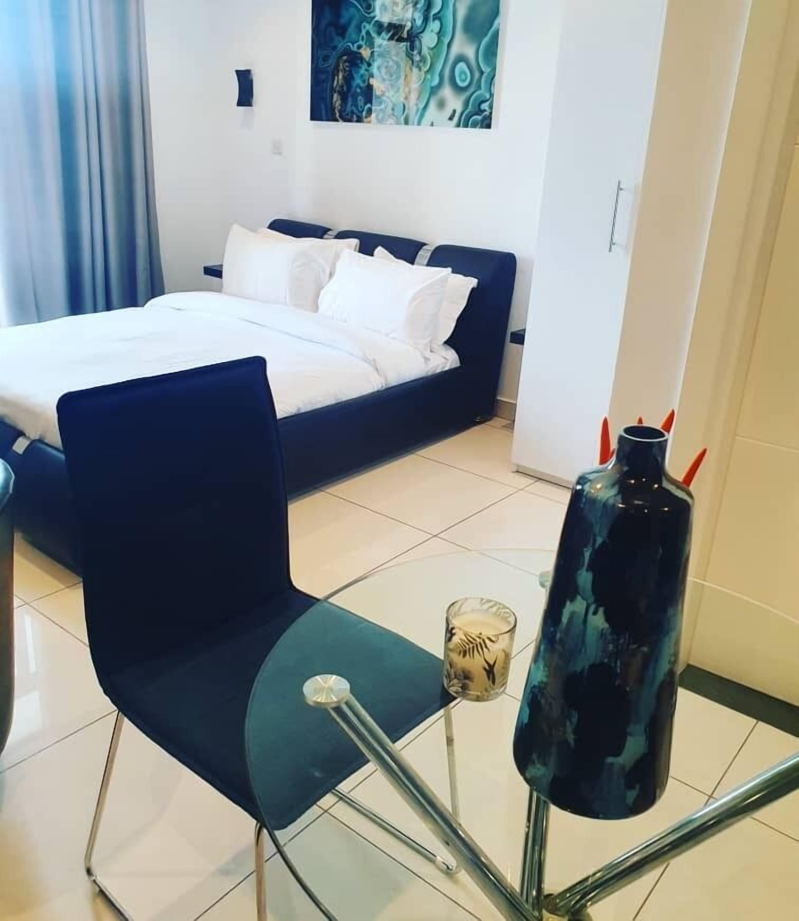 A modern hotel room with a bed, a chair, a table, and a decorative vase.