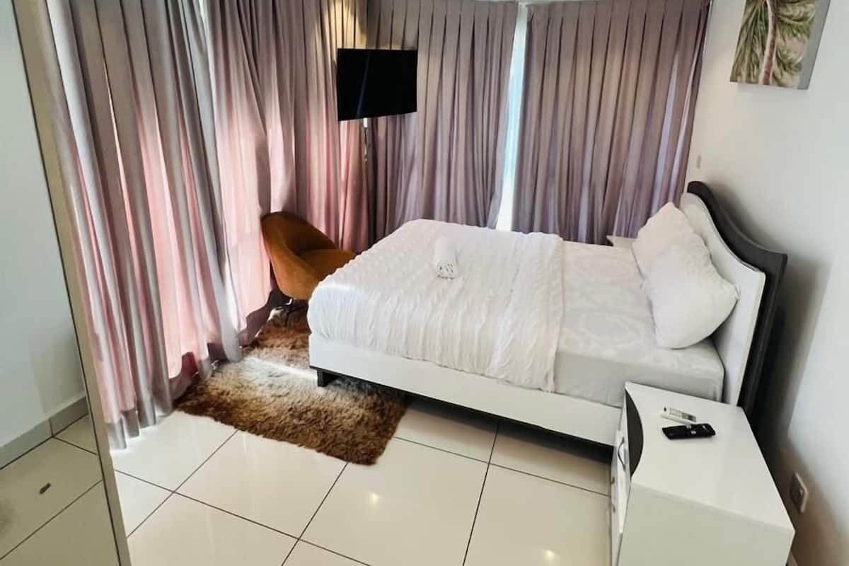 A modern bedroom with a large bed, a flat-screen TV mounted on the wall, and a small bedside table.