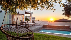 A pool area with a chair, lounge chairs, and a modern building in the background.