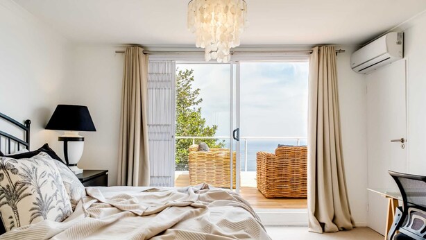 A bedroom with a bed, a nightstand, a lamp, a chair, a desk, and a view of the outdoors through a sliding door.