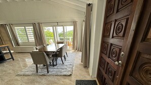 Un espace repas comprenant une table et des chaises, une porte en bois ornée de sculptures complexes, et une vue dégagée grâce à de grandes fenêtres.
