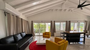 Un salon spacieux avec un canapé noir, des fauteuils jaunes, un tapis rouge et une table à manger.